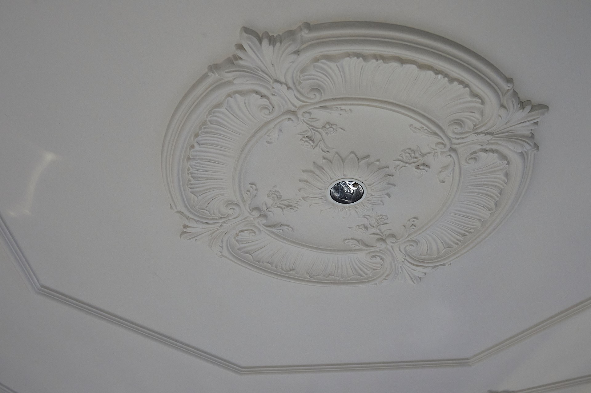Verzierte Rosette mit skulpturalen Details, die die architektonische Deckenverzierung unterstreicht.
