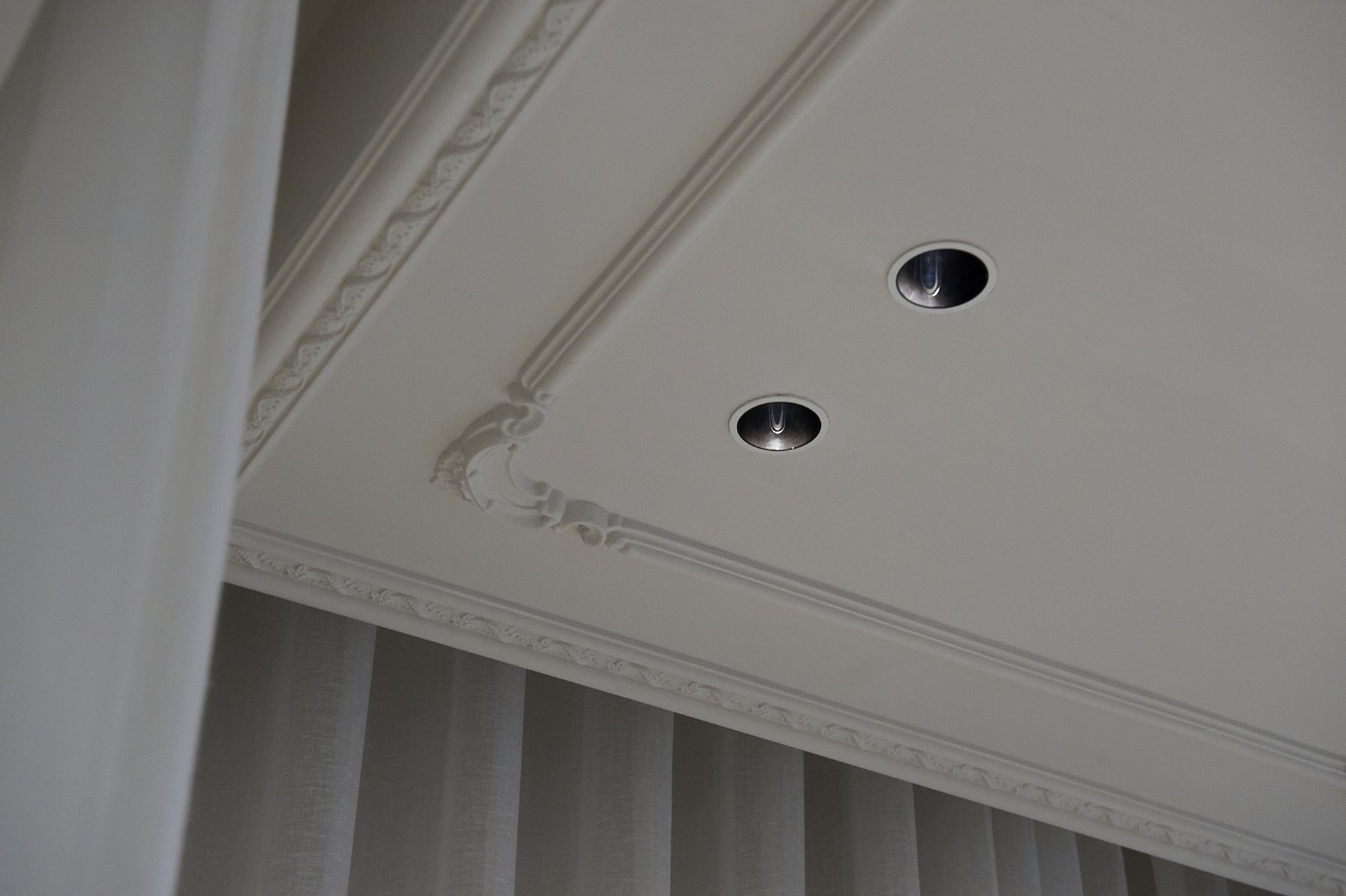 An der Decke angebrachte Wandleisten, die die Einbaustrahler und die Proportionen der Decke betonen.